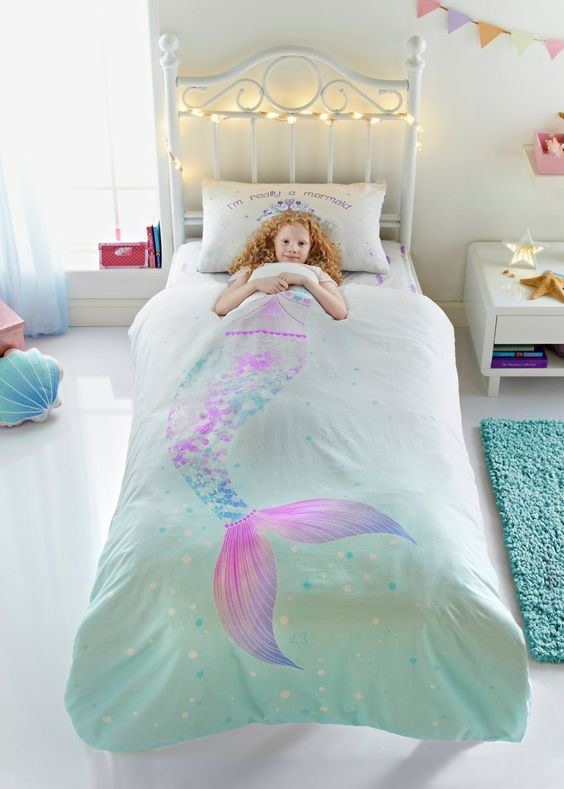 دکوراسیون اتاق خواب کودک دختری که روی تخت سفید آن روتختی طرح پری دریایی پهن شده است